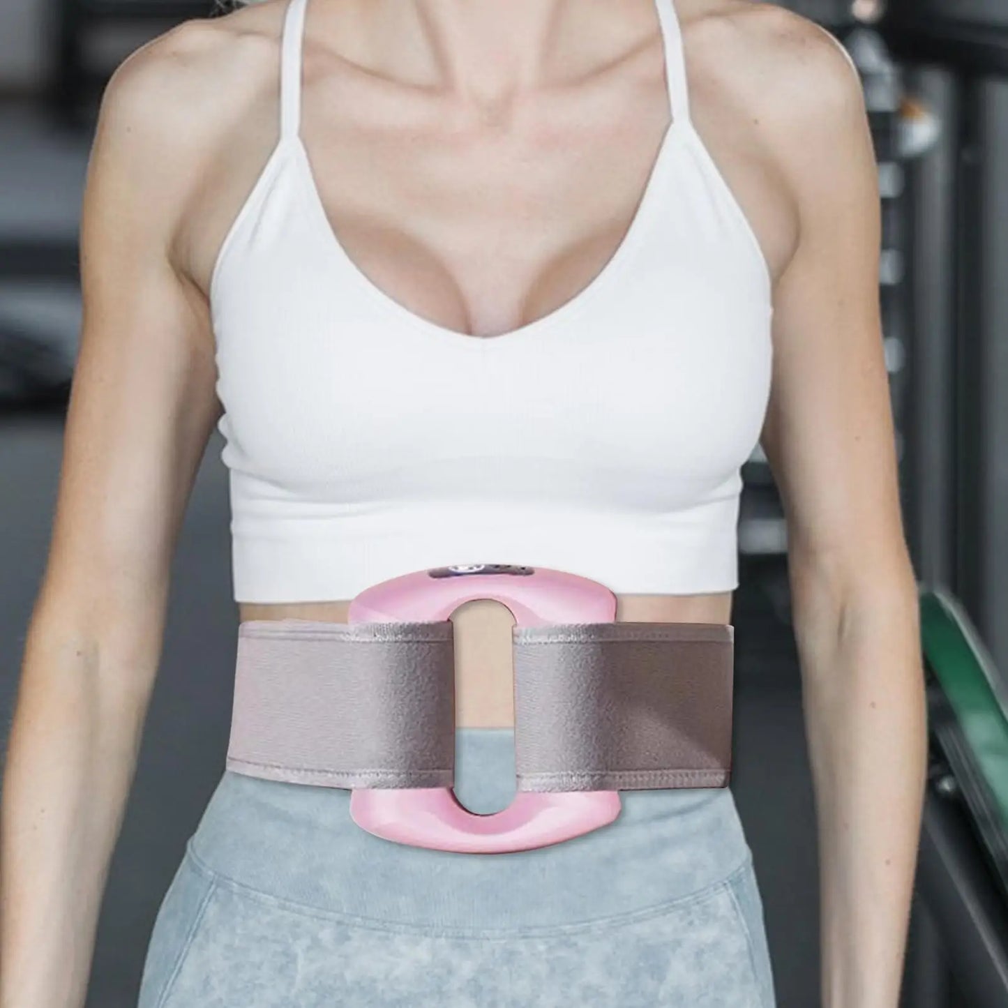 Person wearing a pink and gray waist trainer in a gym setting. مدلك الجسم